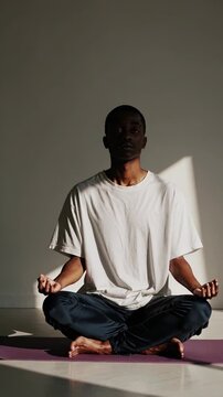 Meditation practice in calm indoor space. Individual performs yoga poses for relaxation and mindfulness. Soft light creates serene atmosphere. Vertical format enhances focus on subject.