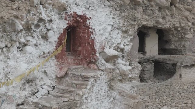Drone sweeps left to right across the facade of an ancient Ladakh monastery carved into the mountainside offering a dramatic view of the intricate stone entrance