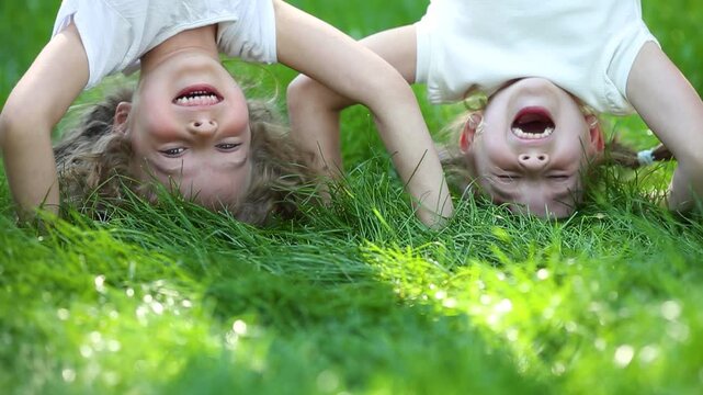 Funny kids do a handstand in a summer park on green grass. Slow motion