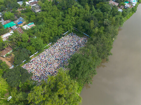 Joypurhat, Bangladesh - 28 May 2026: Aerial view of a large congregation of people praying in an open field beside a river and dense green trees.