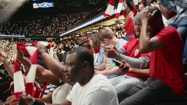 African american fans tracking live score for a bet ticket on mobile app, watching intense football match at the stadium, supporters placing high risk wager on betting app, match update.