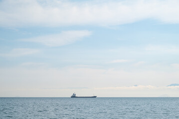 Naklejka premium Lone Cargo Ship on Calm Seto Inland Sea with Soft Blue Sky and Distant Mountains in Japan