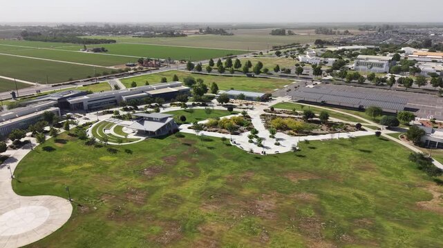 Sunny afternoon aerial view of the College of the Sequoias campus and surrounding urban downtown area, with green agricultural fields expanding towards the horizon in Visalia, California
