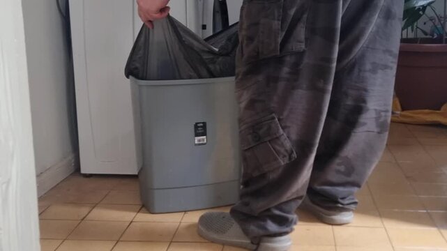 Low angle mare wearing crocs removing rubbish bag from bin in home utility room