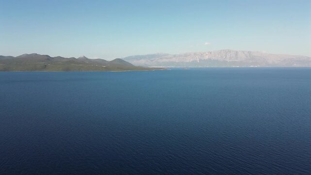 Scenic drone shot over the deep blue waters of the Ionian Sea in Nydri, Lefkada, looking across towards the mainland coast of Preveza under a clear sky. High quality 4K video.