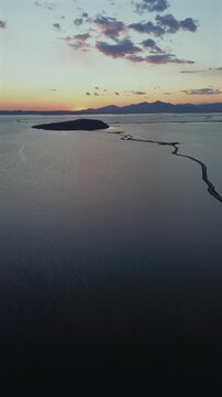 Vertical aerial drone shot of a scenic sunset over the peaceful waters and islets of Koronisia in the Ambracian Gulf, Greece. High quality 4K video for social media.