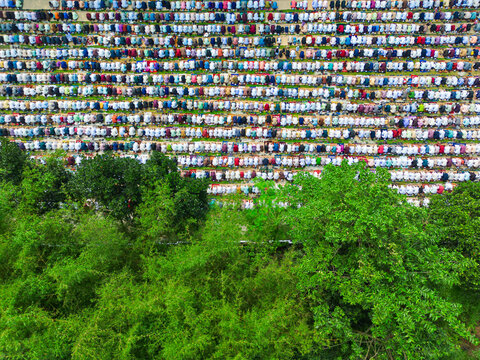 Joypurhat, Bangladesh - 28 May 2026: Aerial view of a large crowd of people gathered for prayer in rows next to lush green trees.