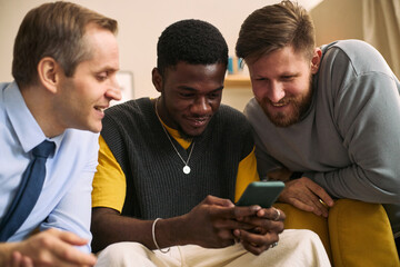 Multiethnic young adult men gathering around smartphone, sharing content and smiling, expressing male friendship and connection. Ideal for social media, community, teamwork marketing