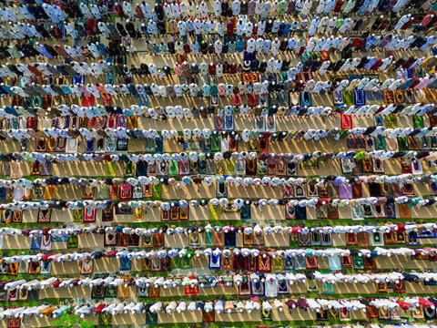 Joypurhat, Bangladesh - 28 May 2026: Aerial view of a large crowd of Muslim men performing Eid prayer in neat rows on colorful mats with long shadows.