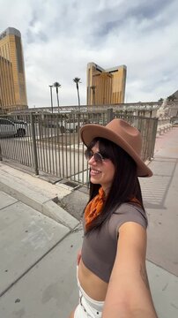 Beautiful young woman wearing a hat and sunglasses taking a selfie video while walking and exploring the famous landmarks on the las vegas strip, enjoying her vacation in nevada