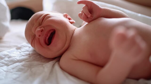 Upset newborn baby crying while lying on a white sheet, expressing intense emotions of discomfort and sadness. The unhappy infant is very fussy, feeling lonely and uncomfortable