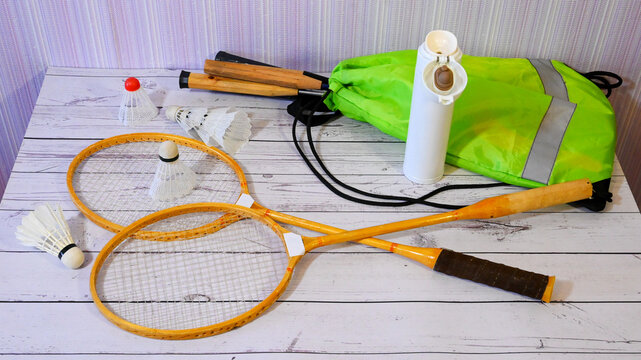 two wooden rackets and shuttlecocks with a jump rope and a green backpack on a light floor