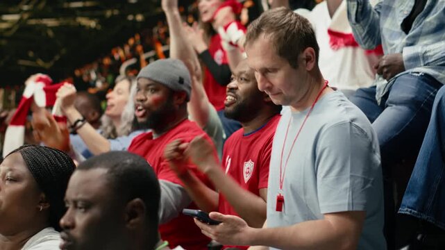 Focused man supporter placing live bet ticket on mobile betting app during football match with cheering crowd at the stadium, fan living high risk betting odds with tension, in-play prediction.