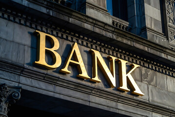 Fototapeta premium Gold letters spelling BANK are mounted on the stone facade of a large building.