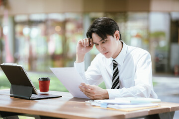 Fototapeta premium Young professional reviewing documents at an outdoor workspace, showing concern about employment, financial matters, career decisions, and business challenges.