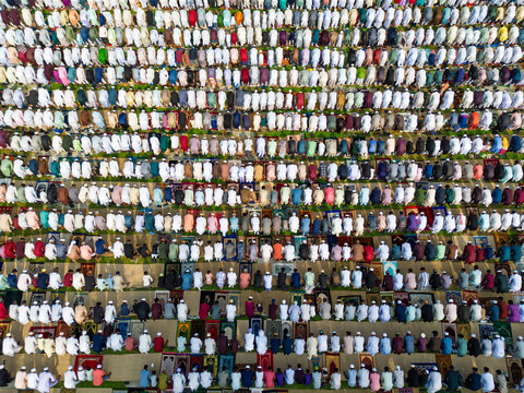 Joypurhat, Bangladesh - 28 May 2026: Aerial view of a large crowd of Muslim men performing prayer on colorful rugs in neat rows during a religious gathering.