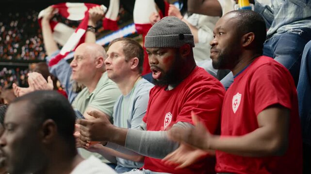 Passionate black fans following live betting odds on smartphone, cheering during exciting football match at stadium with sports betting pressure.