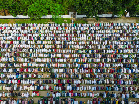 Joypurhat, Bangladesh - 28 May 2026: Aerial view of a large crowd of Muslim men gathered in neat rows for prayer on colorful mats outdoors near green trees.