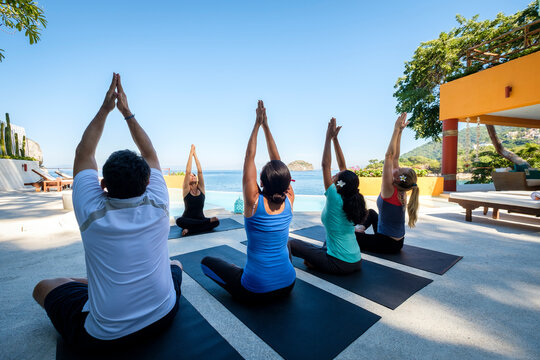 Yoga group with teacher exercising at ocean front villa