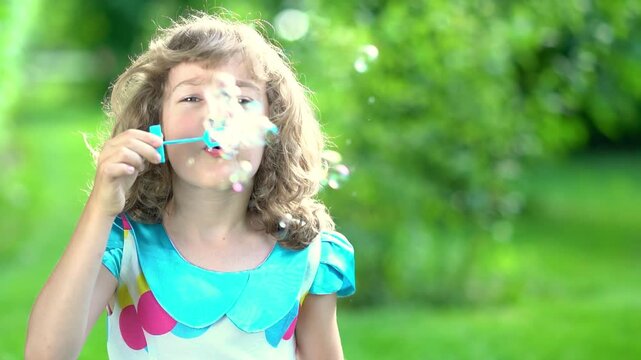 A happy child blows soap bubbles in a summer park. Slow motion