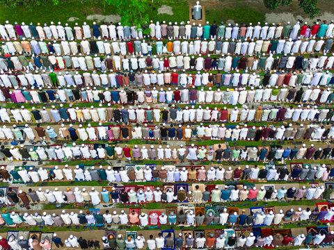 Joypurhat, Bangladesh - 28 May 2026: Aerial view of a large crowd of Muslim men performing Eid al-Adha prayers in neat rows on colorful mats in an outdoor field.