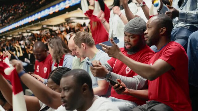 African american fans tracking live score for a bet ticket on mobile app, watching intense football match at the stadium.
