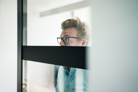 Wide-eyed businessman behind glass pane in office