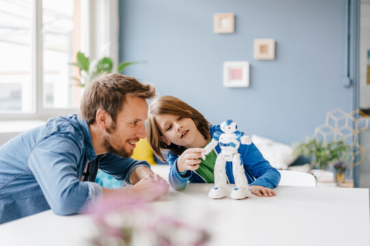 Happy father and son playing with robot on table at home