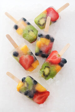 Six fruit ice lollies with fresh fruits on white ground