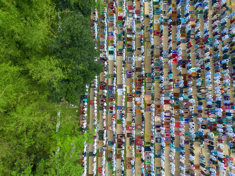 Joypurhat, Bangladesh - 28 May 2026: Aerial view of a large crowd of people praying in rows on colorful rugs next to lush green trees during a religious gathering.