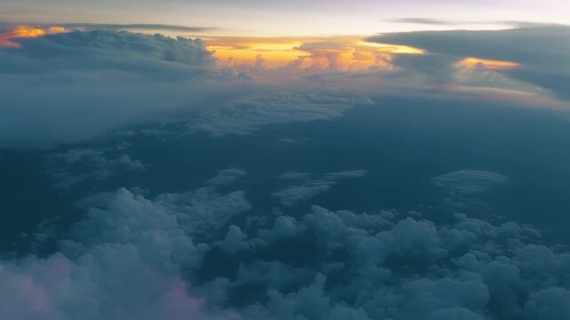 Breathtaking aerial view above dense cloud layers during sunset with vibrant golden and orange light breaking through. Dark blue atmospheric tones create dramatic contrast below.
