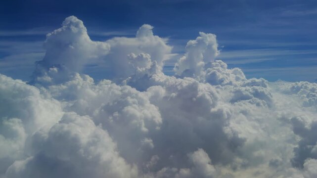 Dramatic aerial view of towering cumulus clouds rising majestically against a deep blue sky. Fluffy white cloud formations create stunning cloudscape with wispy cirrus streaks in the upper atmosphere.