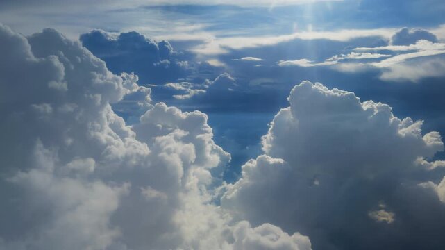 Stunning aerial view flying above massive white cumulus clouds with golden sunbeams piercing through the deep blue sky. Dramatic cloudscape shows billowing formations and light rays.