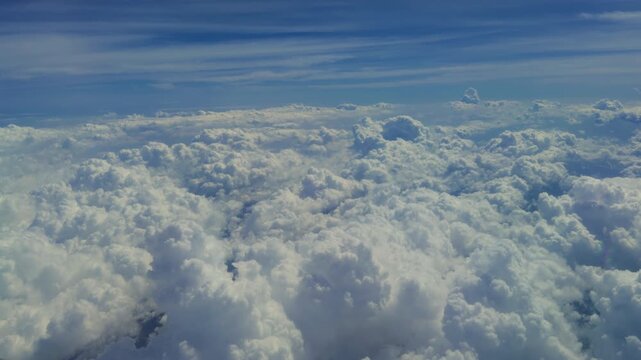 Aerial view above thick white cumulus clouds stretching across the horizon under a deep blue sky. Soft puffy cloud formations create a peaceful dreamlike atmosphere from airplane altitude.
