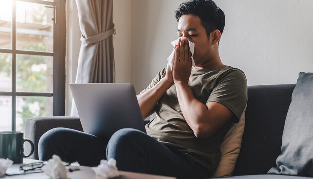 Man Sneezing While Working on Laptop at Home Office