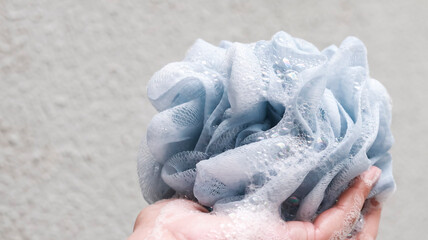 Fototapeta premium A close-up shot of a hand holding a soft, blue mesh bath sponge filled with white soap bubbles and lather, highlighting a relaxing personal hygiene and skincare routine.