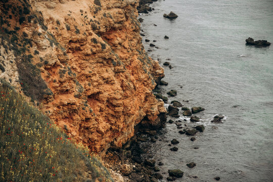 Red limestone cliff above calm sea with rocky shoreline wild coastal grass soft cloudy light natural geology landscape seaside travel tourism erosion layers and dramatic nature view
