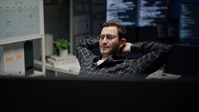 Tired developer with glasses stretch arms on chair to relief fatigue, programmer taking break from computer cyber security work late at night.
