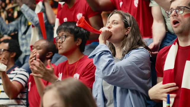 Passionate woman football supporter cheering with red team crowd in stadium stands during intense live soccer match, football equality and inclusion, sports fans celebrate with chants.