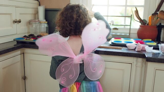 Child, baking and butterfly wings in kitchen, development and learn culinary skills with ingredients. Kid, growth and girl with creative costume, cooking and dessert preparation with recipe in house