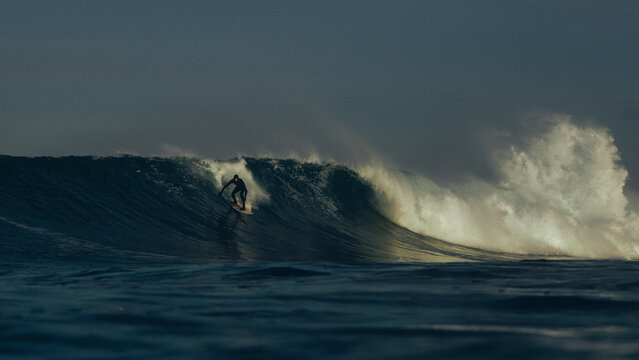 surfer taking off on large wave at sunrise