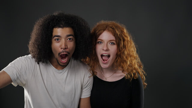 Young man and woman opening mouths in surprise, reacting to shocking news