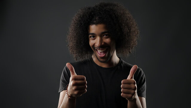Young black man smiling and giving double thumbs up on a dark background
