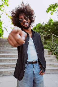 Smiling man with afro hair and sunglasses pointing directly at camera outdoors at park.