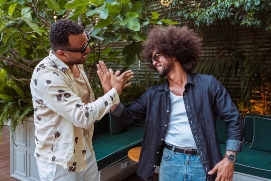 Two smiling latin american men high fiving, celebrating friendship and achievement in a lush outdoor setting.