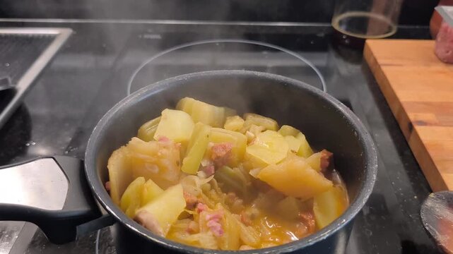 Top down view of a boiling cardoon and potato stew steaming in a pot on an induction hob