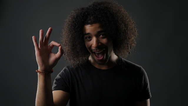 Excited man with curly hair making an okay gesture while looking at camera