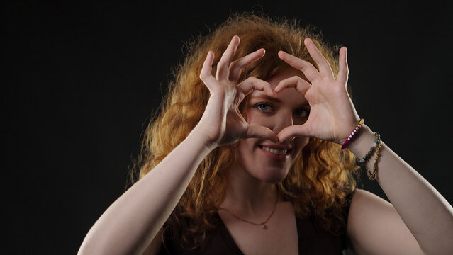 Smiling woman forming heart shape with fingers, showing love and happiness