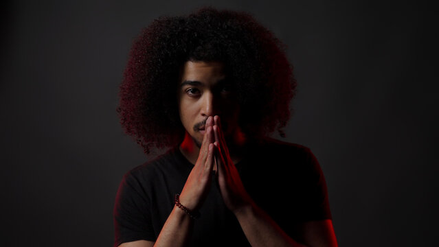 Young man with Afro hair praying with hands together, reflecting on spiritual thoughts