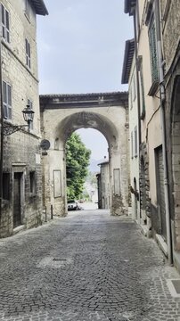 Vicolo storico in pietra con edifici antichi, finestre con persiane e arco panoramico sullo sfondo, ideale per progetti dedicati a borghi europei, turismo
